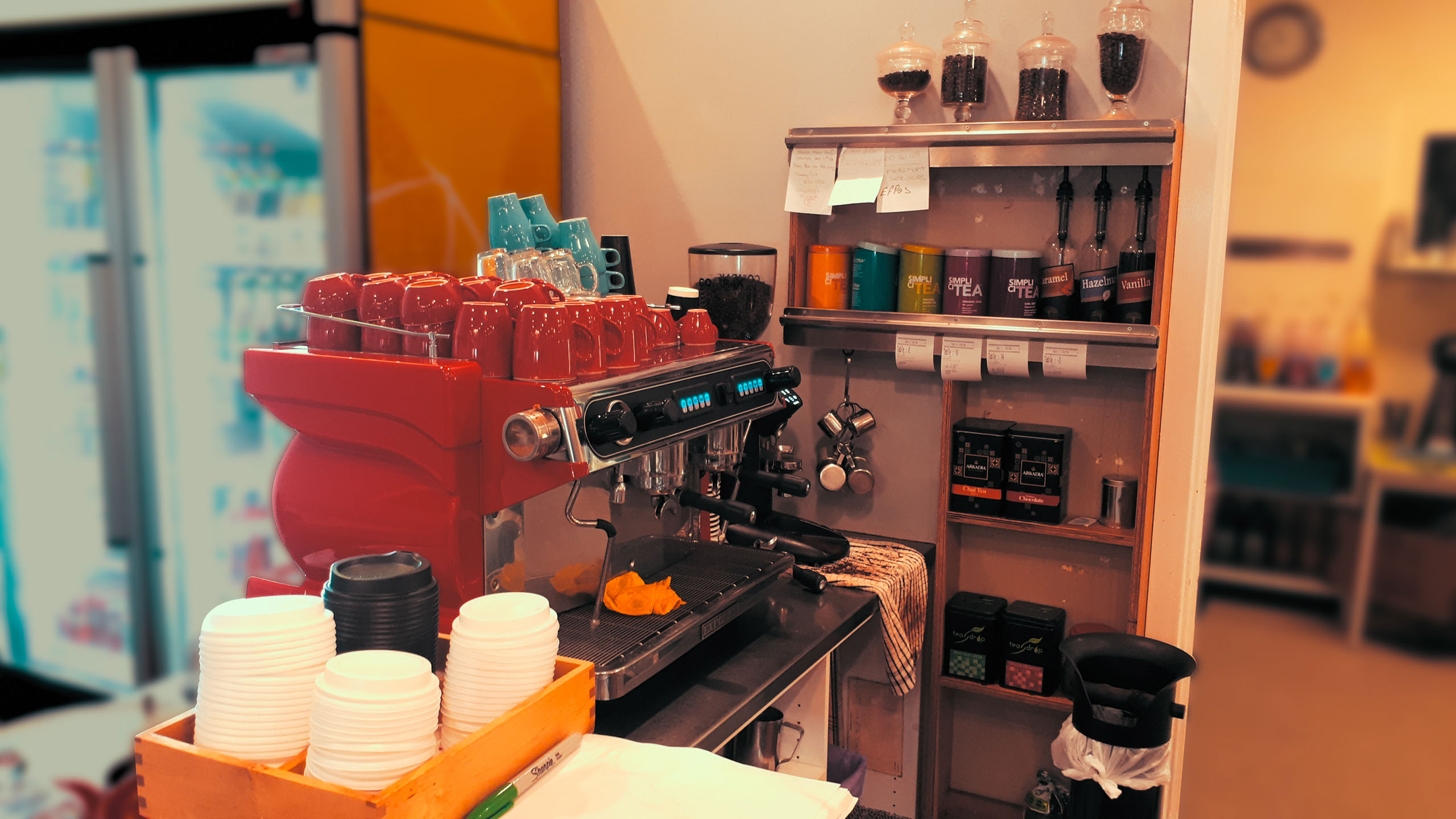 A a big red coffee shop coffee machine with mugs on top.